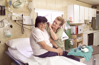 Woman sitting on a medical bed getting her ears checked by a health care worker