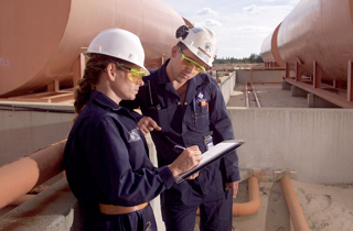 A man and a woman wearing Cameco coveralls and hard hats looking at a clipboard together